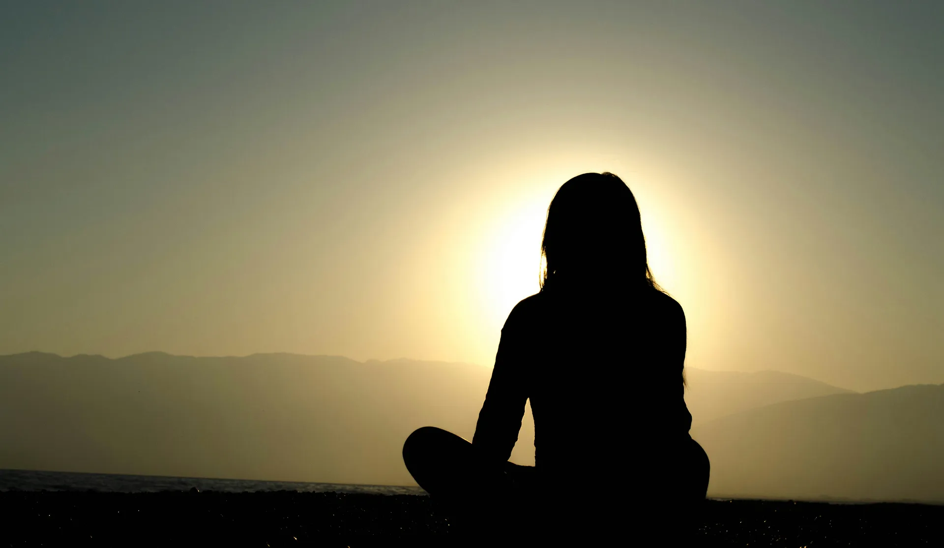 Mujer meditando en la montaña frente al sol